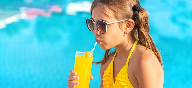 The child is drinking a cocktail by the pool