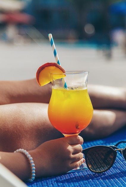 The child is drinking a cocktail by the pool