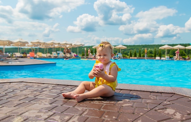 The child is eating ice cream near the pool. Selective focus. Kid.