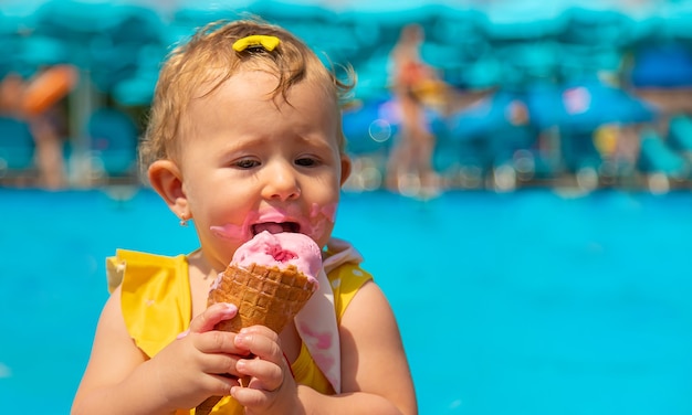 The child is eating ice cream near the pool. Selective focus. Kid.