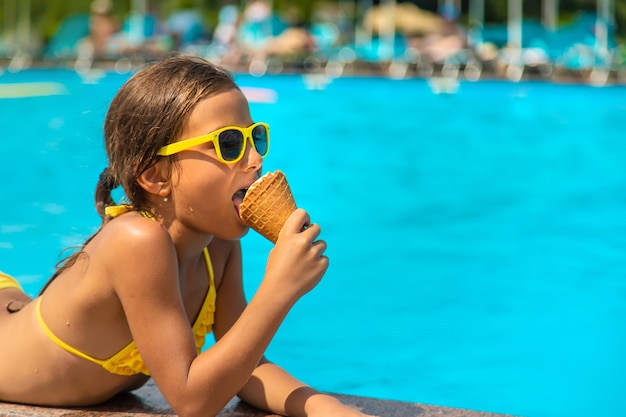 The child is eating ice cream near the pool. Selective focus.