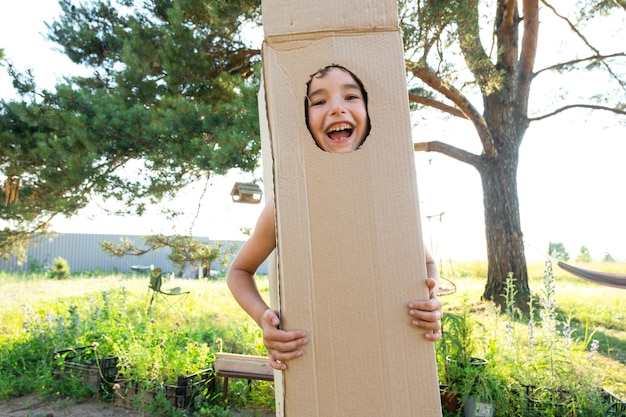 The child is funny dancing and fooling around in a box costume round cutout for face and hands Moving to a new house children's games from improvised means a suit with your own hands