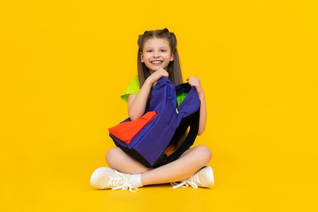 The child is going to school sitting A little girl is rummaging through a school backpack Additional education for schoolchildren Preparatory courses for children Yellow isolated background