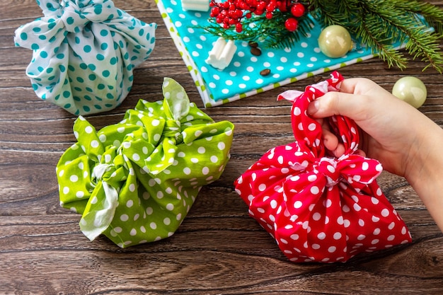 Il bambino tiene in mano i regali di natale anno nuovo e confezioni regalo furoshiki zero rifiuti sul tavolo di legno