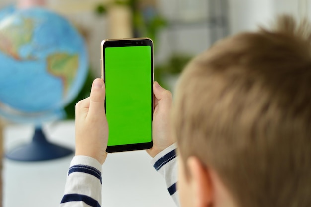 The child is holding a phone in his hand with a green screen