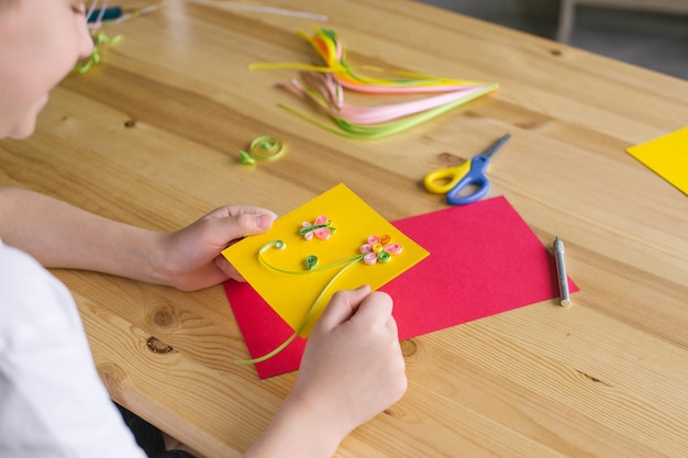 The child is holding a postcard for mom made by his own hands quilling