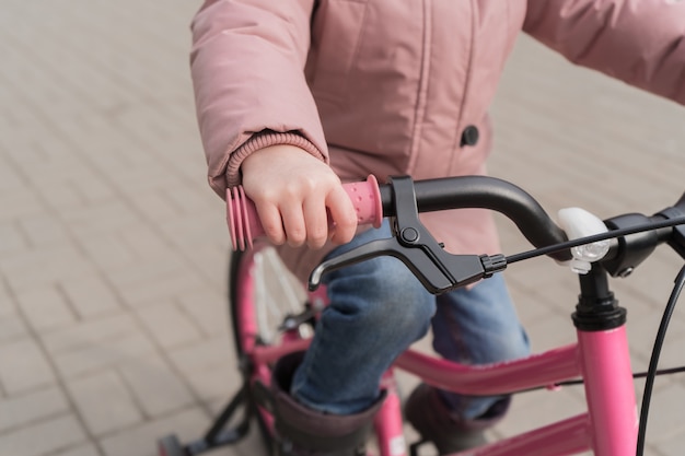 子供は自転車の車輪を握っています。ピンクのジャケットを着た女の子が自転車に乗っています。