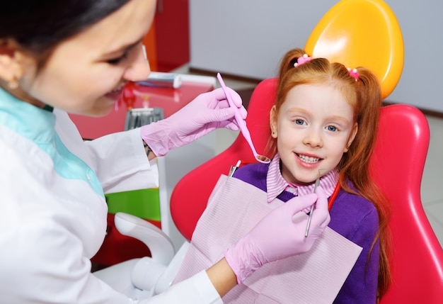 Foto il bambino è una bambina dai capelli rossi che sorride seduto su una poltrona del dentista.