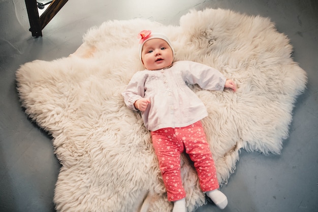 The child is lying on a woolen carpet and smiles at the camera