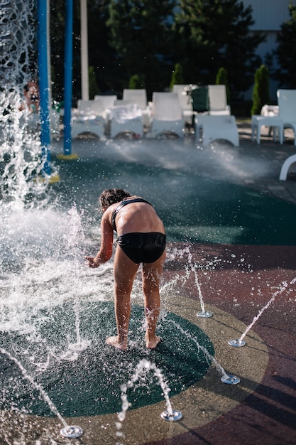 子供が噴水で遊んでいる小さな女の子が噴水に寄りかかって水しぶきを楽しんでいます...