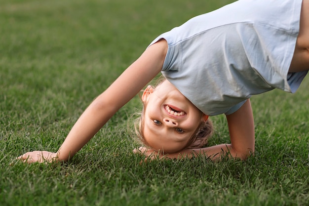 子供は草の上で遊んでいます逆さまに立ち上がろうとしている小さな女の子