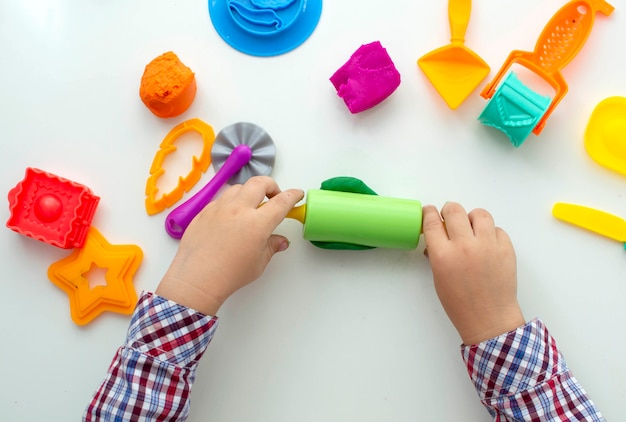 Child is playing with game test on white table. he has lot of\
toys on table. molds, dough roller and scissors. children\'s\
creativity. development of the concept of fine motor skills.\
selective focus.