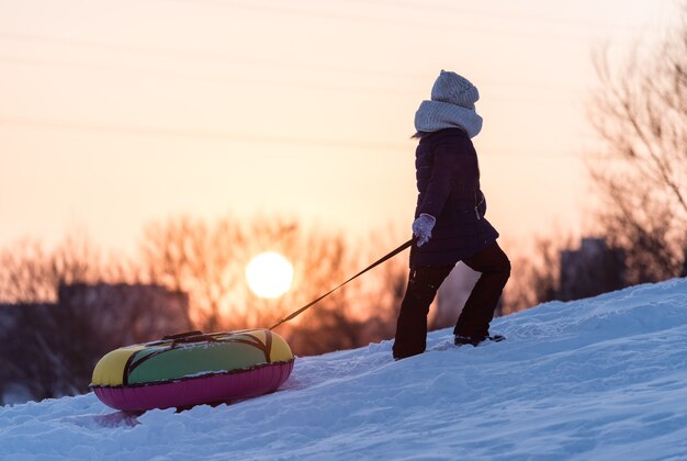 A child is pulling tubing on a snowy mountain at sunset