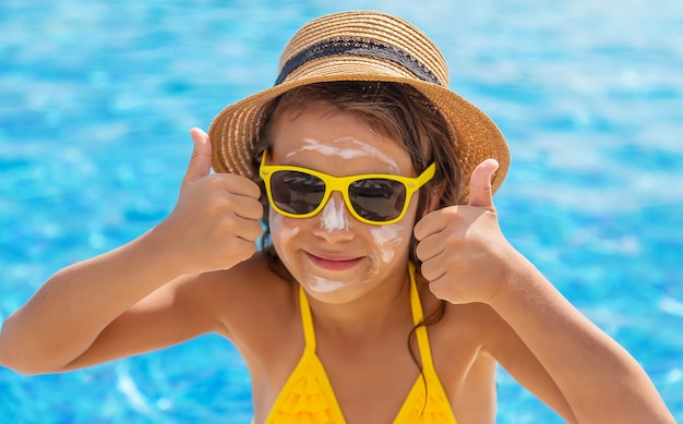 The child is putting sunscreen on her face. Selective focus. Kid.