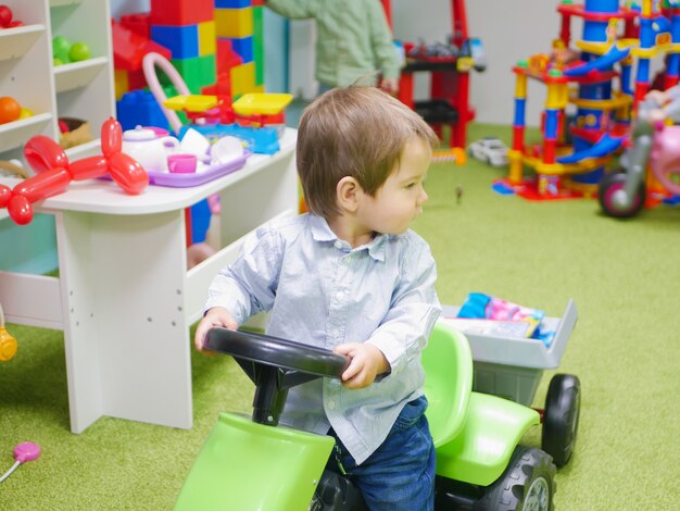 子供はおもちゃの車に乗っています。子供が家でおもちゃで遊んでいます。幼い子供は幼稚園でおもちゃで遊ぶ。おもちゃの車の少年