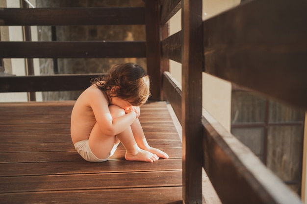 Il bambino è triste abbraccia le ginocchia e stringe un bambino in mutandine bianche si siede e si gode il sole estivo