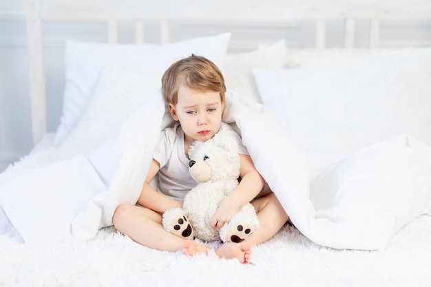 A child is sad with a teddy bear on the bed at home