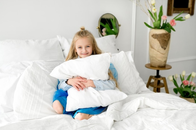 Foto il bambino è seduto nel letto con lenzuola bianche come la neve abbracciando un grande cuscino morbido