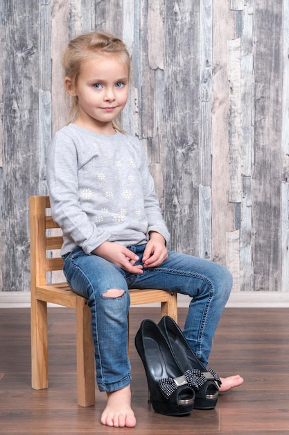 child is sitting on a chair and prepared to put on her mother high-heeled shoes