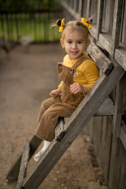 한 아이가 농장 뒤뜰에 있는 닭장 근처 사다리에 앉아 있다