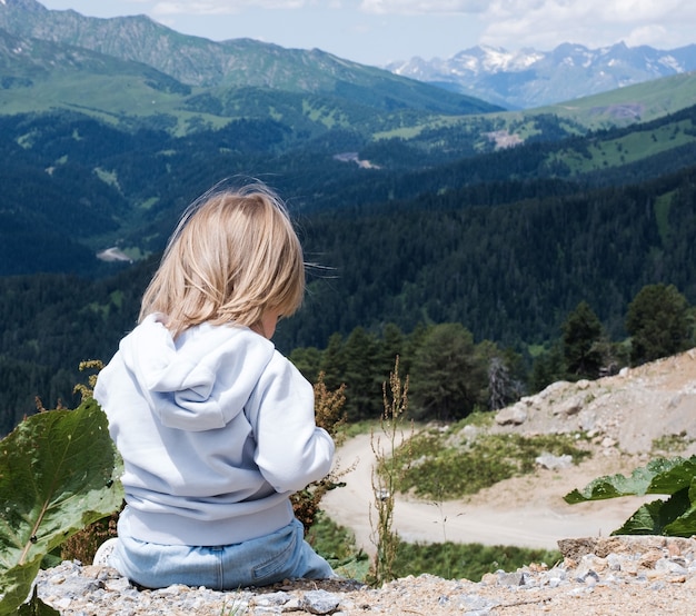 子供は座ってコーカサス山脈の風景を見ていますアウトドア旅行地元の旅行