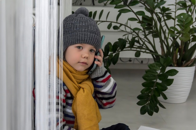 子供は暖かいセーターと帽子を着てヒーターの近くに座って、手形を手にお金と電話を持っています 危機の概念と公共事業の大規模なセット