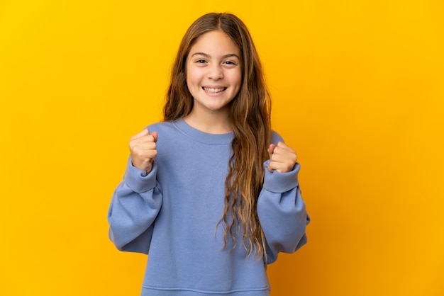 Photo child over isolated yellow background celebrating a victory in winner position
