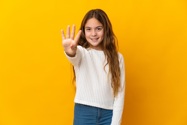 Ребенок на изолированном желтом фоне счастлив и считает четыре пальцами