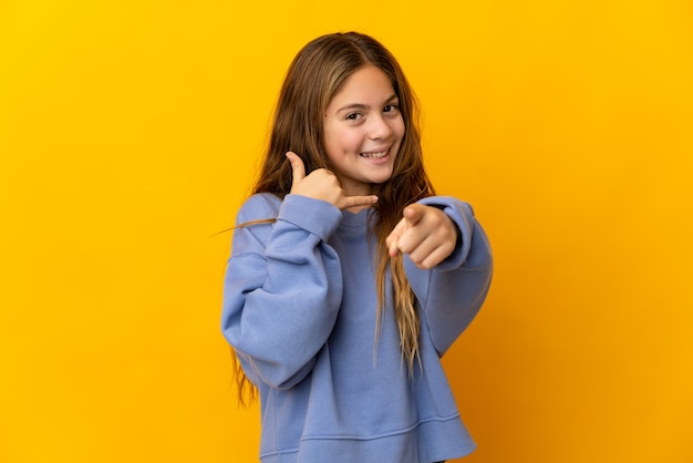 Child over isolated yellow background making phone gesture and pointing front