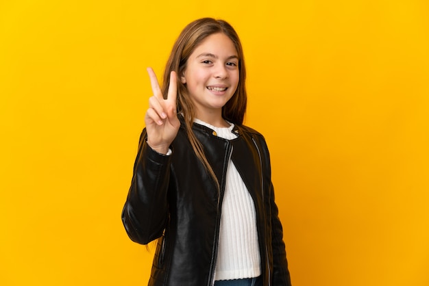 Child over isolated yellow background smiling and showing victory sign