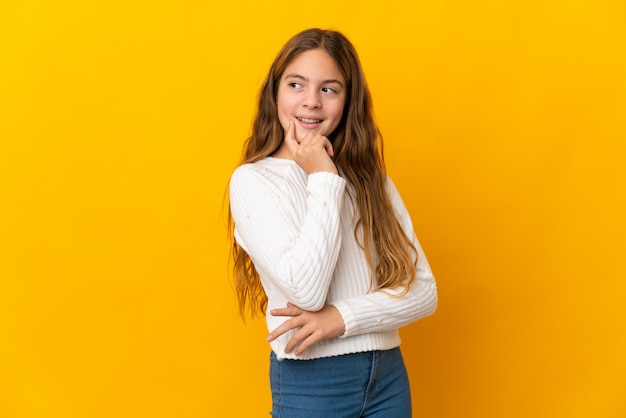 Child over isolated yellow background thinking an idea while looking up