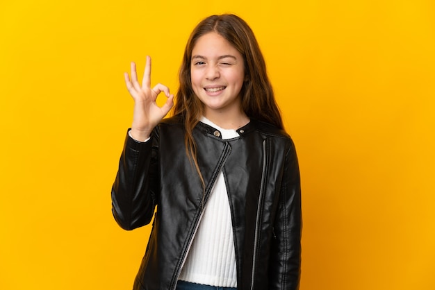 Child over isolated yellow showing ok sign with fingers