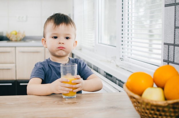 The child in the kitchen, drinking orange juice, close on background of fruits