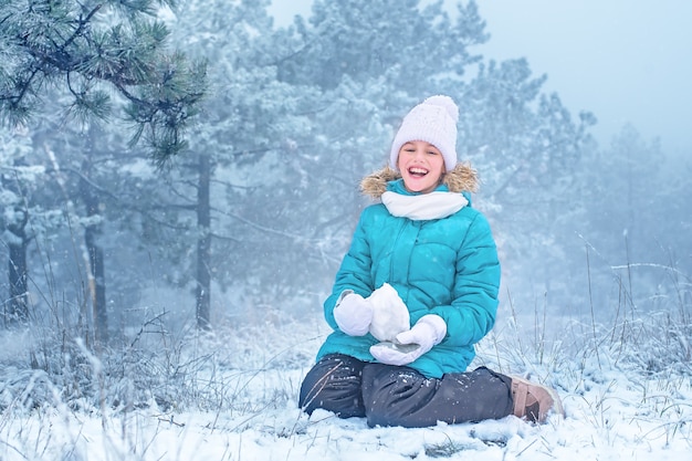 The child laughs and sculpts from the snow. The girl in the snow. Winter fun.