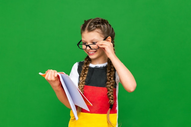 A child learns German on a green isolated background A beautiful little girl with glasses with a German flag and notebooks on a green isolated background