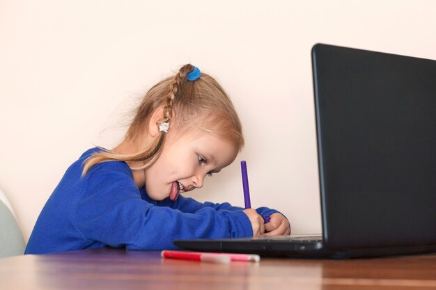 Child learns remotely in front of computer and writes by pen