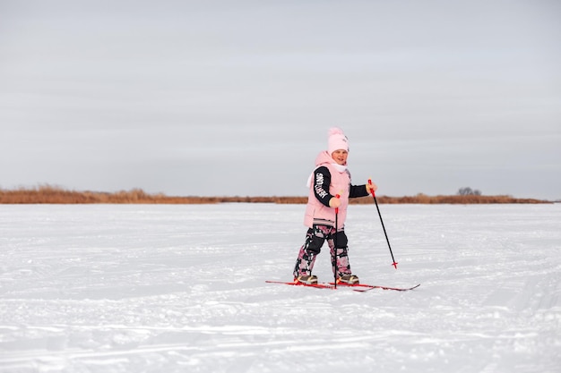 Child learns to ski Little girl in pink warm suit skiing in snow on frosty winter day side view snow background