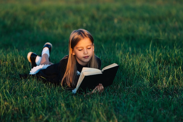 A child lies on the grass and reads a book in the sunset light.