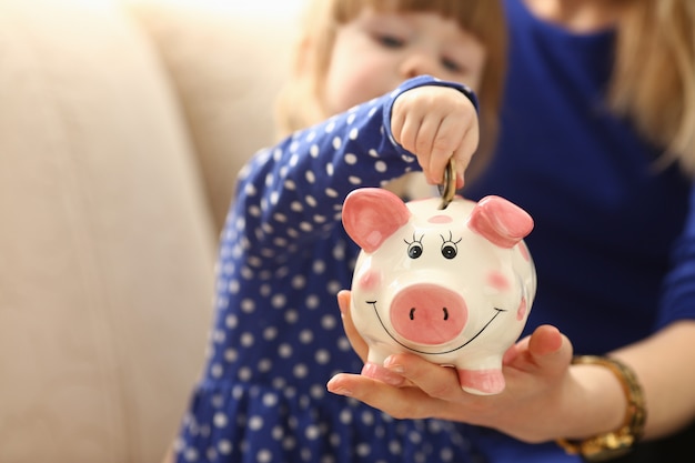 Child little girl arm putting coins into piggybank