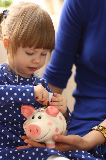 貯金箱にコインを入れる子供の小さな女の子の腕