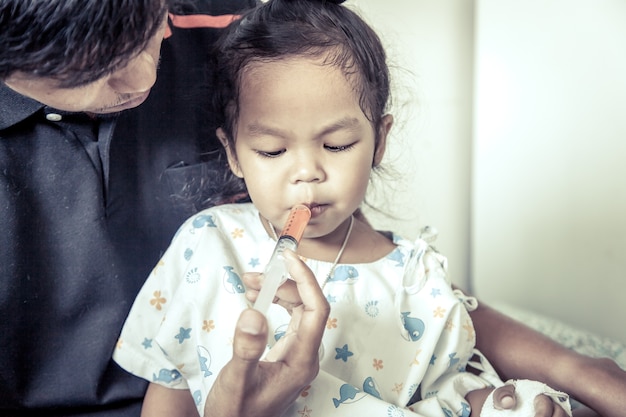 Маленькая девочка получает лекарство со шприцем во рту в старинном цветовом тоне