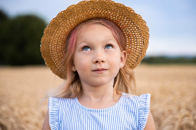 帽子をかぶった小さな女の子が麦畑を背景に見上げる