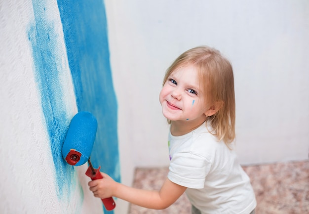 子供、少女はローラーの壁を青で塗る