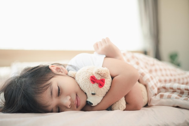 子供の小さな女の子はおもちゃのテディベアと一緒にベッドで寝ています