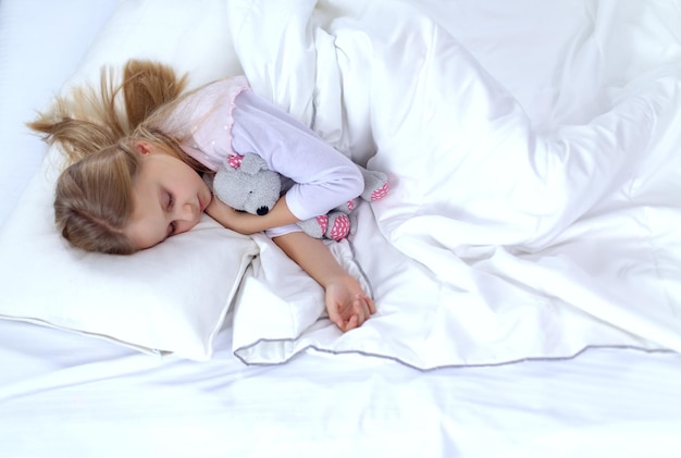 Child little girl sleeps in the bed with a toy teddy bear