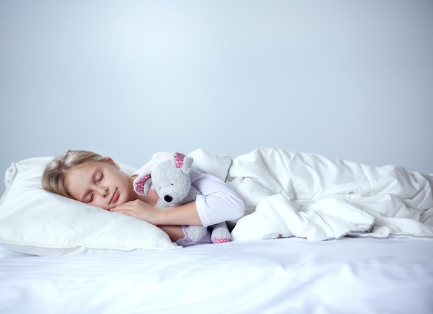 Child little girl sleeps in the bed with a toy teddy bear