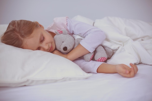 Child little girl sleeps in the bed with a toy teddy bear