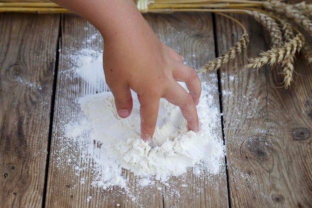 Child little hand with flour and wheat ears on the old table