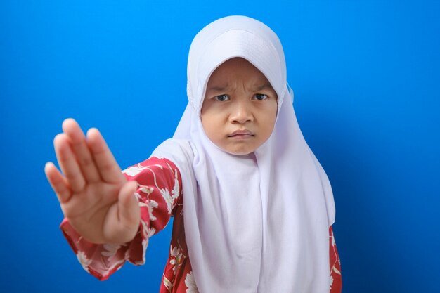 Child looking at camera. Stop signal with her hand. over blue background