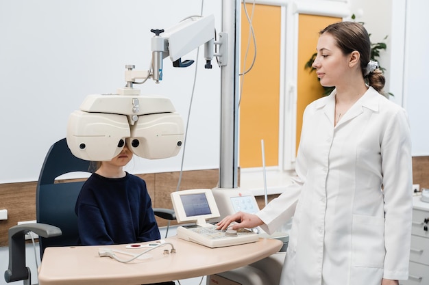 어린이는 굴절 이상을 측정하고 안경 처방을 위한 정보를 결정하기 위해 소아 안과 의사 포롭터의 시력 검사 중에 포롭터를 들여다봅니다.